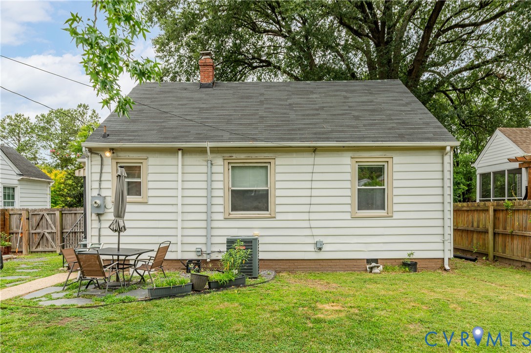 White siding exterior with a shingle roof, brick chimney, and a stone patio