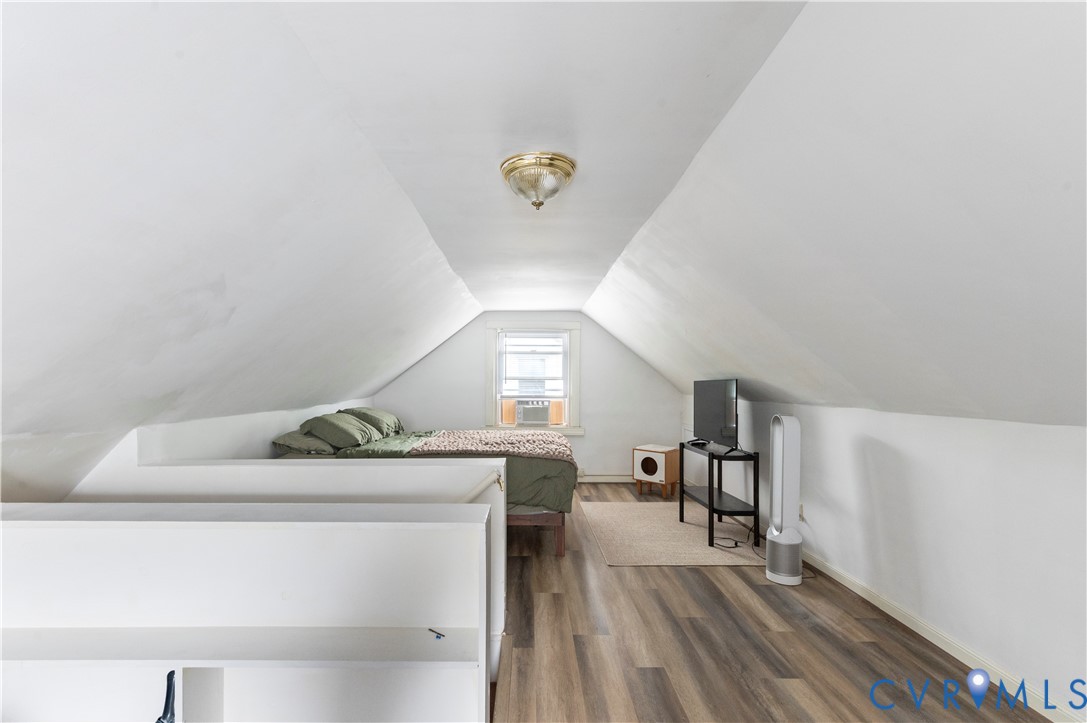Sloped ceiling room featuring wood-finish flooring, a window with an air conditioning unit, and a flush mount light fixture
