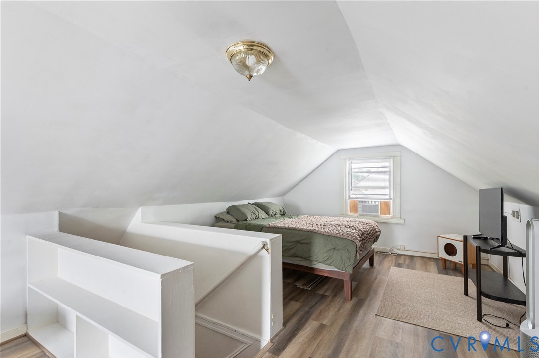 Attic space with sloped ceilings, a single window, overhead lighting, and wood-finish flooring