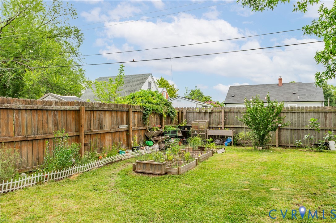 Expansive green space featuring a wood privacy fence, raised garden beds, and mature perimeter trees