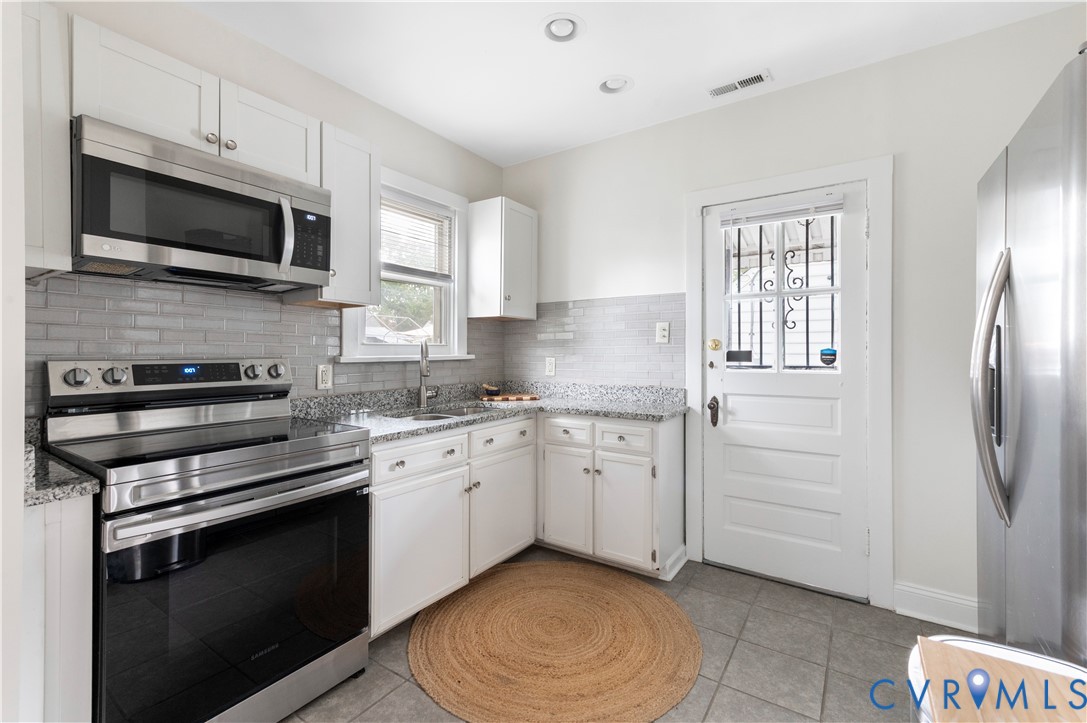 Kitchen featuring white cabinetry, stainless steel appliances, granite countertops, and a tiled backsplash Kitchen featuring white cabinetry, stainless steel appliances, granite countertops, and a tiled backsplash