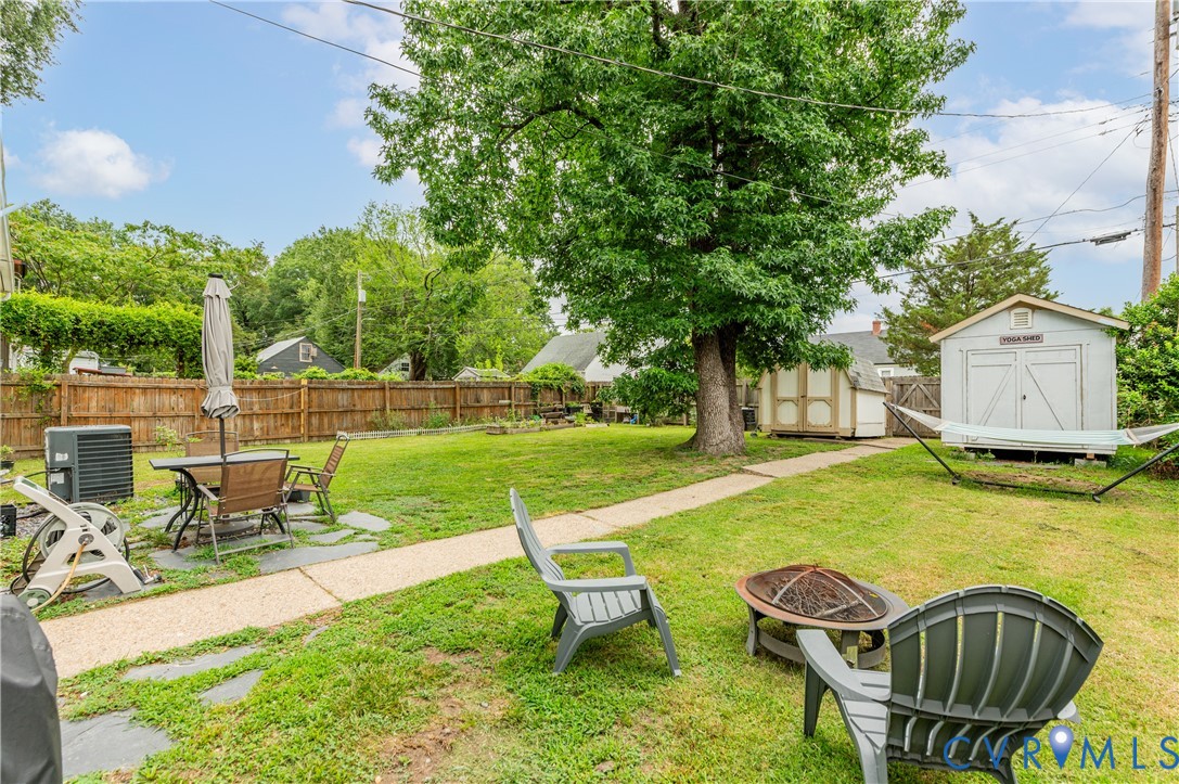 Expansive backyard featuring a manicured lawn, established shade trees, a stone pathway, a wooden privacy fence, and multiple storage sheds