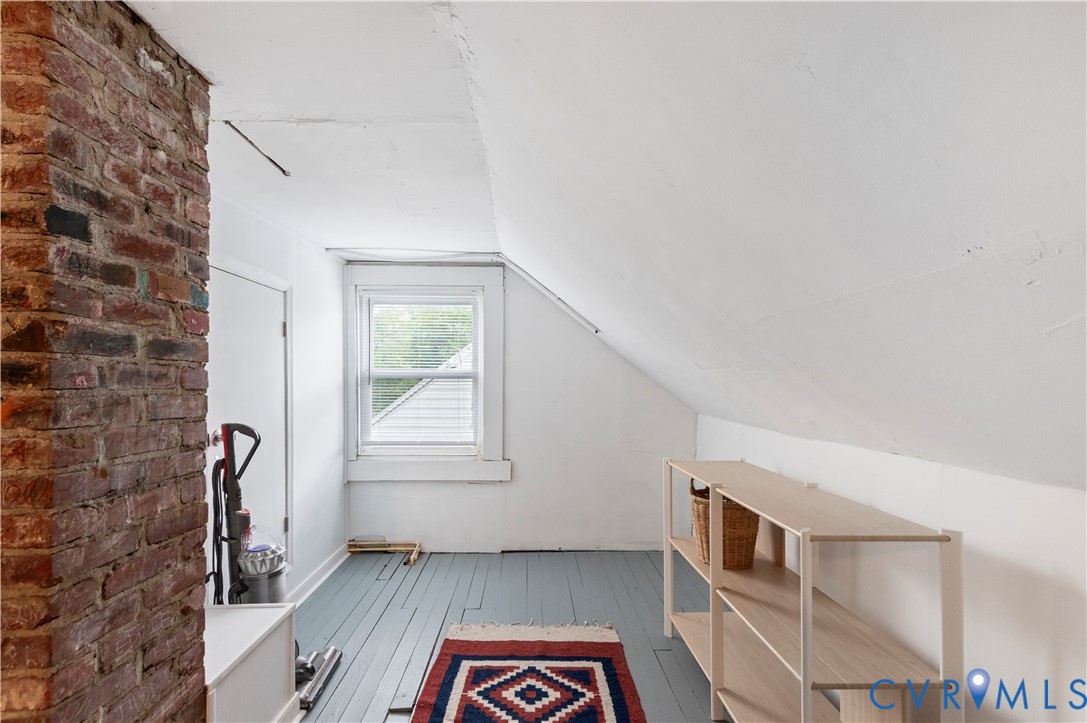 Exposed brick column, painted wood-finish flooring, white sash window, white sloped ceilings, and built-in shelving