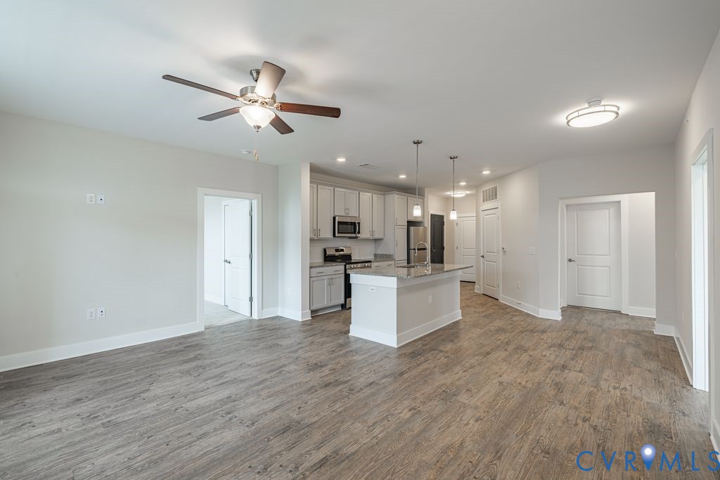 Open-concept living space featuring wood-finish flooring, a contemporary kitchen with light cabinetry, stainless steel appliances, and a central island with pendant lighting