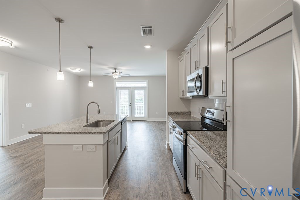 Kitchen featuring a large island with an undermount sink, granite countertops, wood-finish flooring, white cabinetry, and stainless steel appliances