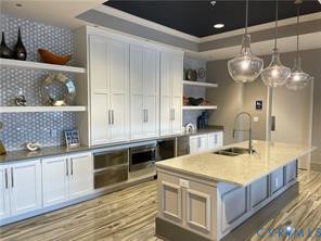 White shaker cabinetry, light-toned countertops, wood-finish flooring, integrated stainless steel appliances, and clear glass pendant lighting