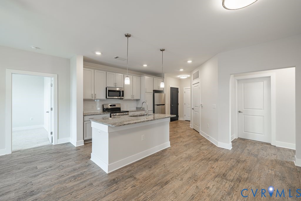 Kitchen island with pendant lighting, stainless steel appliances, light-toned cabinetry, wood-finish flooring, and recessed lighting