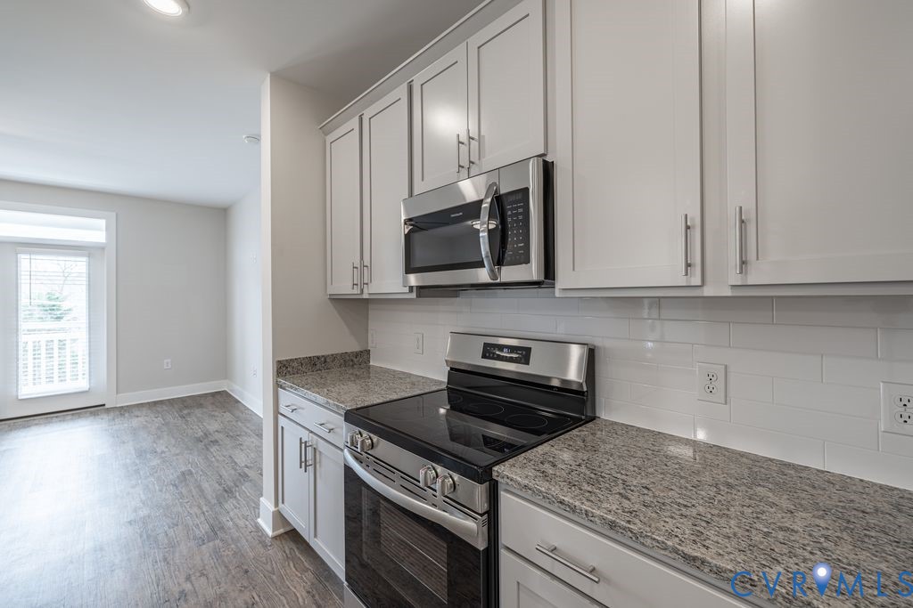 Kitchen featuring light gray cabinetry, stainless steel appliances, speckled countertops, and a white subway tile backsplash