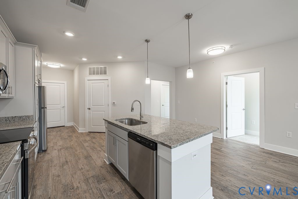 Kitchen featuring an island with a built-in sink, stainless steel appliances, wood-finish flooring, recessed lighting, and pendant lighting