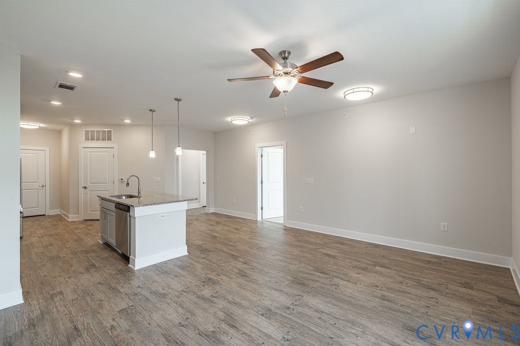 Open concept living area featuring wood-finish flooring, a kitchen island with stone countertop, stainless steel appliances, and a ceiling fan with integrated lighting