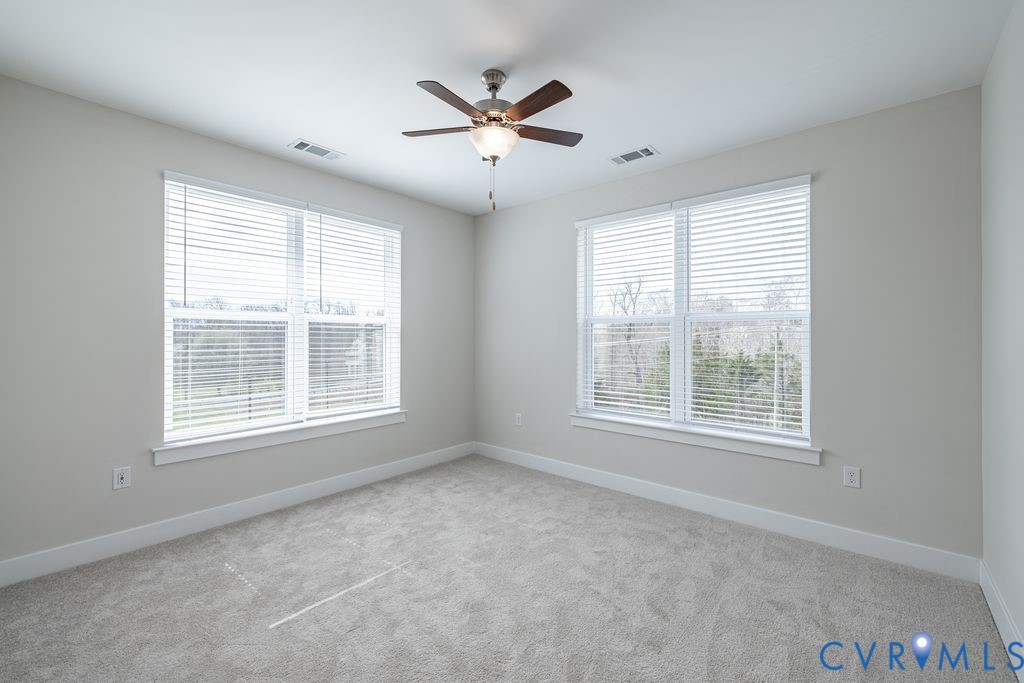Light gray wall paint, two large windows with blinds, ceiling fan, and gray carpeting