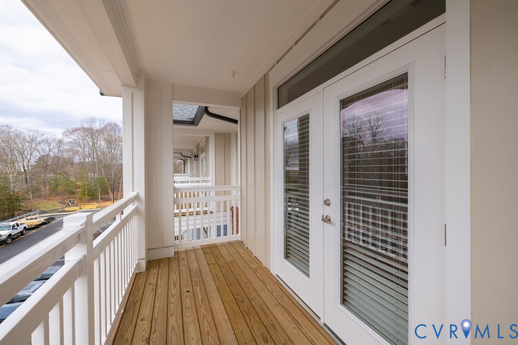 Outdoor balcony featuring wood-finish flooring, white railing, and double French doors with integrated blinds