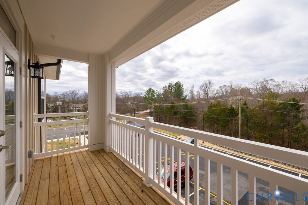 Balcony with wood-finish flooring, white railing, exterior wall sconce, and French door access