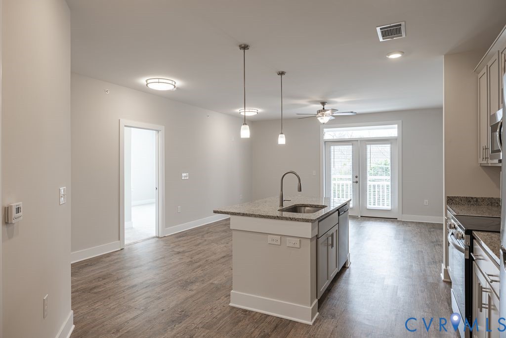 Spacious room featuring wood-finish flooring, a kitchen island with sink, pendant lighting, ceiling fan, and double patio doors