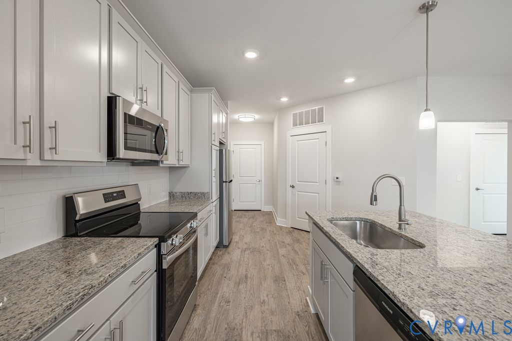 Kitchen featuring wood-finish flooring, white cabinetry, stainless steel appliances, speckled countertops, and a subway tile backsplash