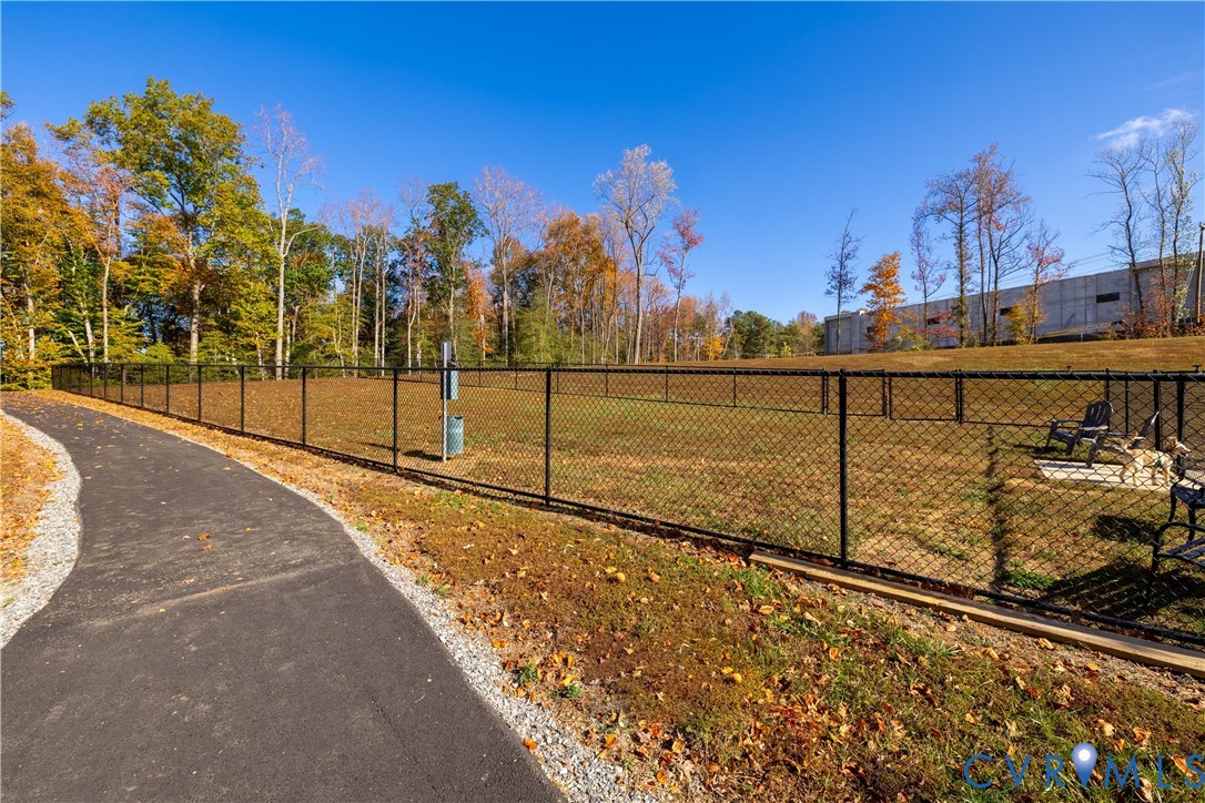 Fenced Dog Park featuring a paved path, natural landscaping, and a chain-link enclosure