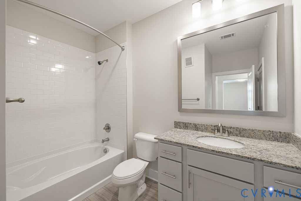 Bathroom featuring a built-in tub with white subway tile surround, a single vanity with a light-colored countertop, and wood-finish flooring
