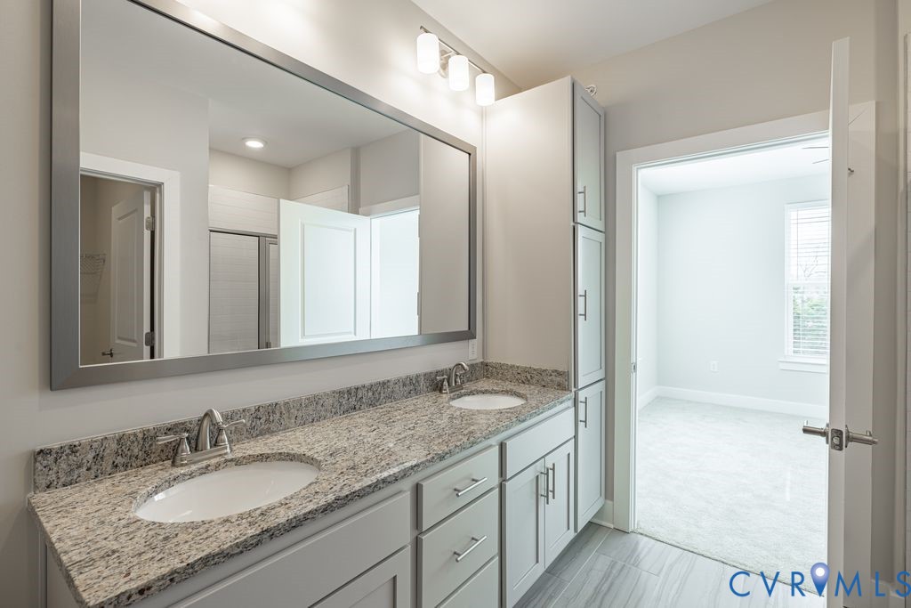 Dual vanity with light-toned cabinetry, granite countertop, and integrated sinks
