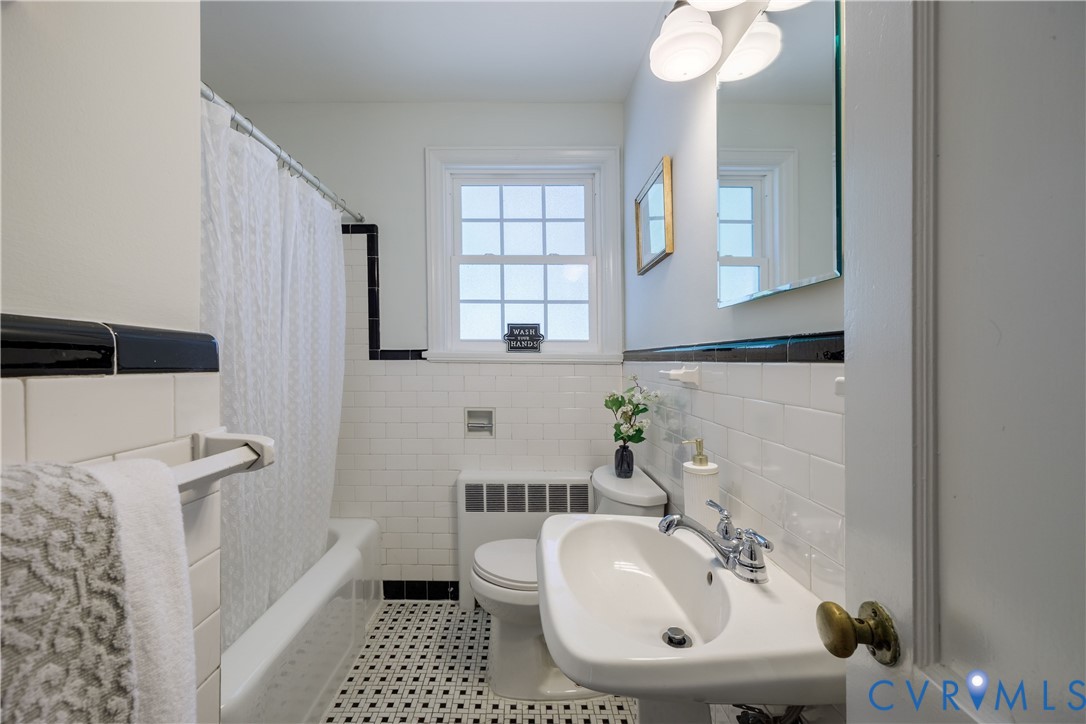 White subway tile walls with black trim, pedestal sink, chrome fixtures, built-in tub with shower, and checkered floor tile