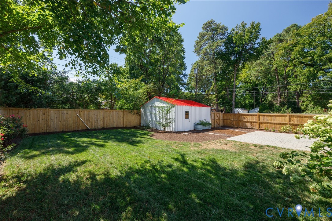 Private backyard featuring a wood privacy fence, a storage shed with a red roof, a paver patio, and a grass lawn