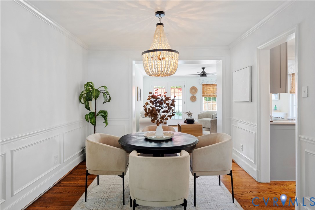 Hardwood flooring throughout, elegant beaded chandelier, white wainscoting, crown molding, and a wide cased opening