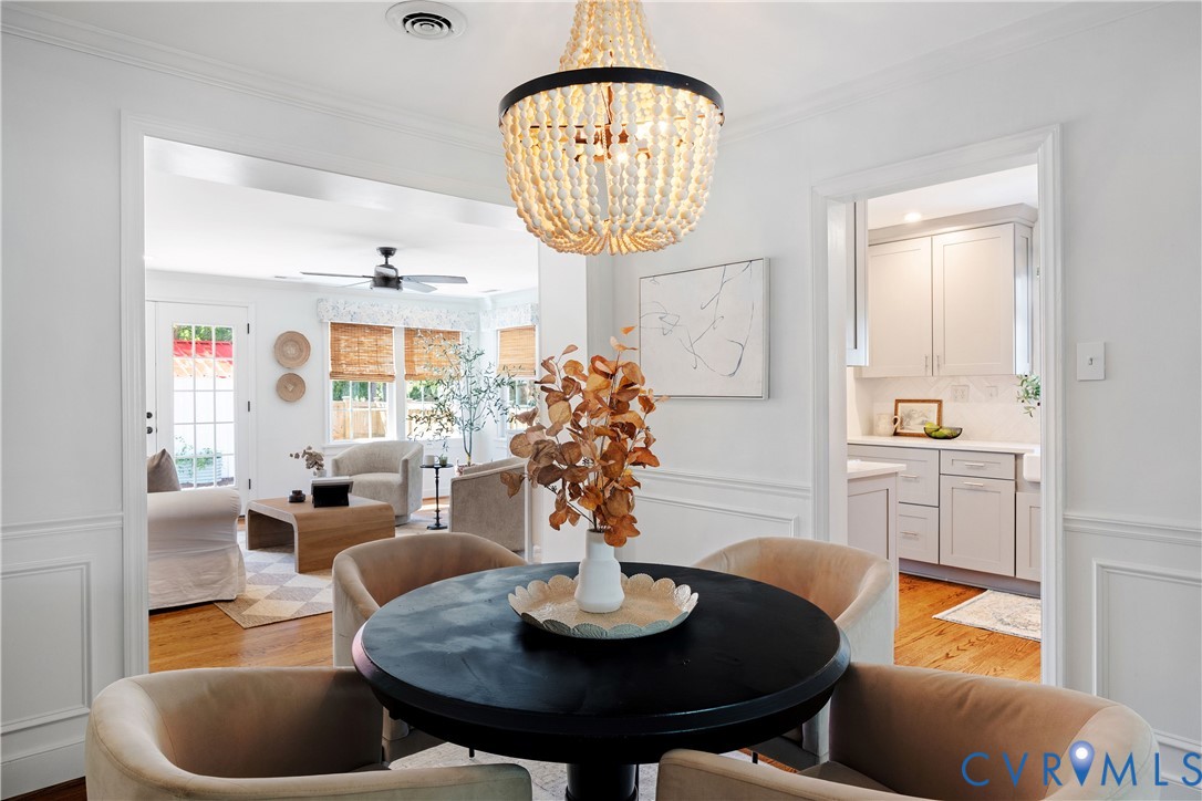 Wainscoting and crown molding details, wood-finish flooring, a beaded chandelier, and a recessed kitchen