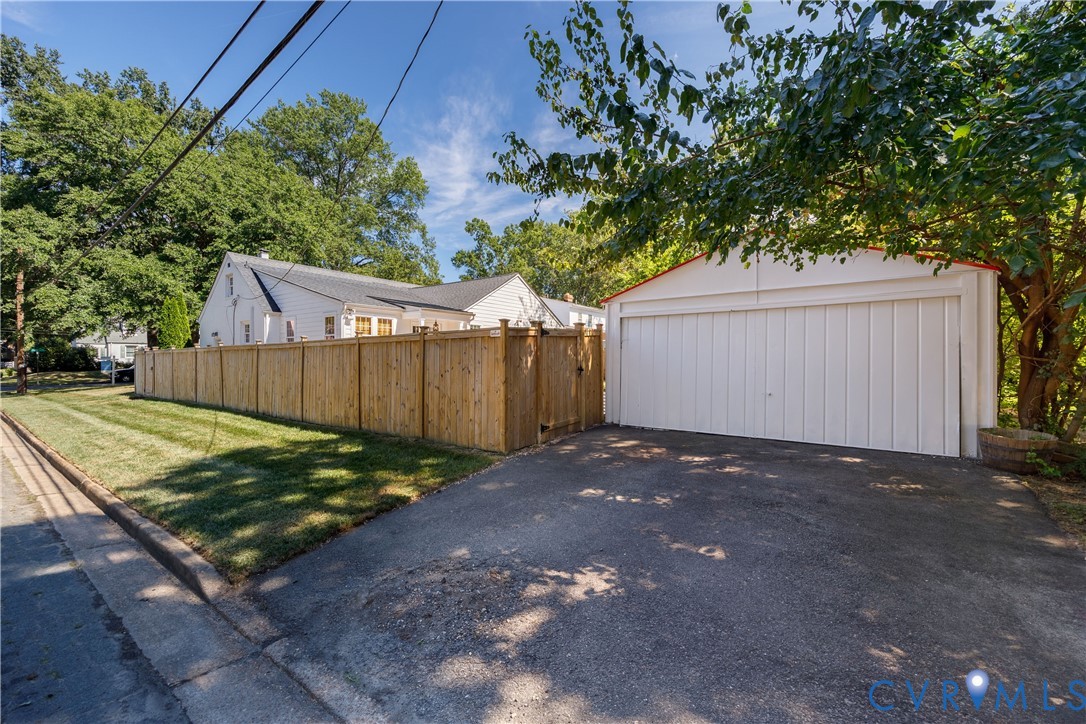 Detached two-car garage with white paneled door, asphalt driveway, and wood privacy fence