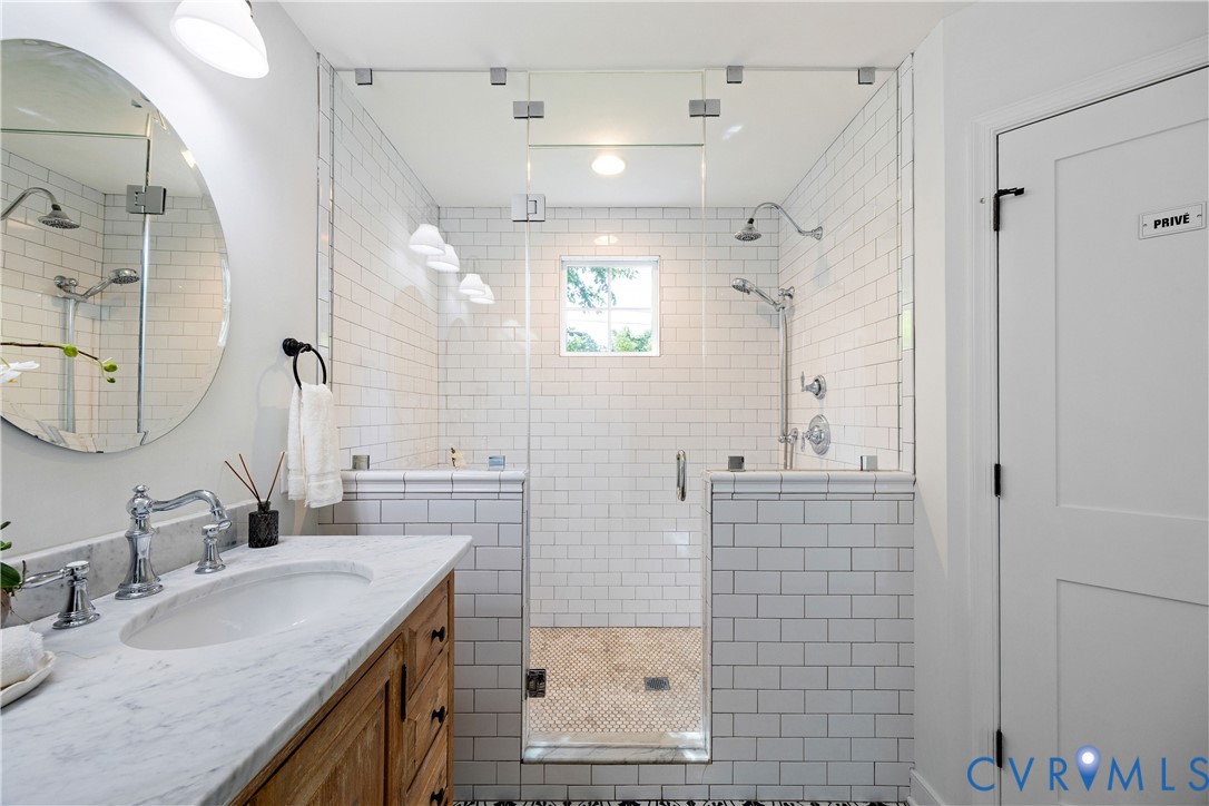 White subway tile shower with glass enclosure, dual showerheads, and a mosaic tile floor