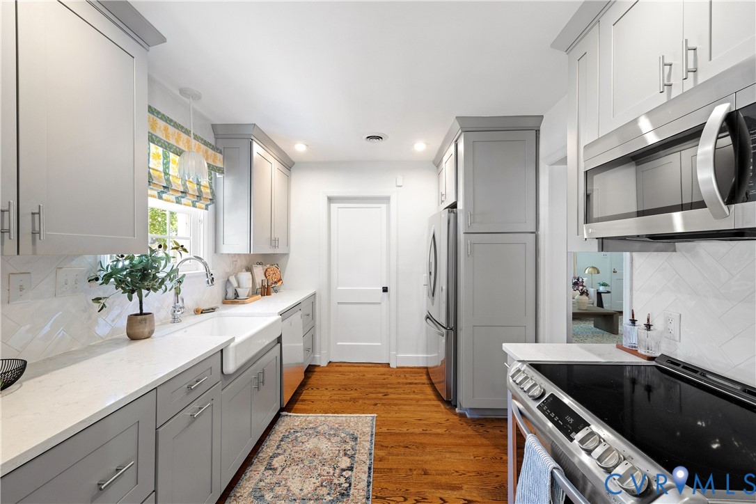 Galley kitchen featuring wood-finish flooring, white countertops, two-tone cabinetry, a farmhouse sink, and stainless steel appliances