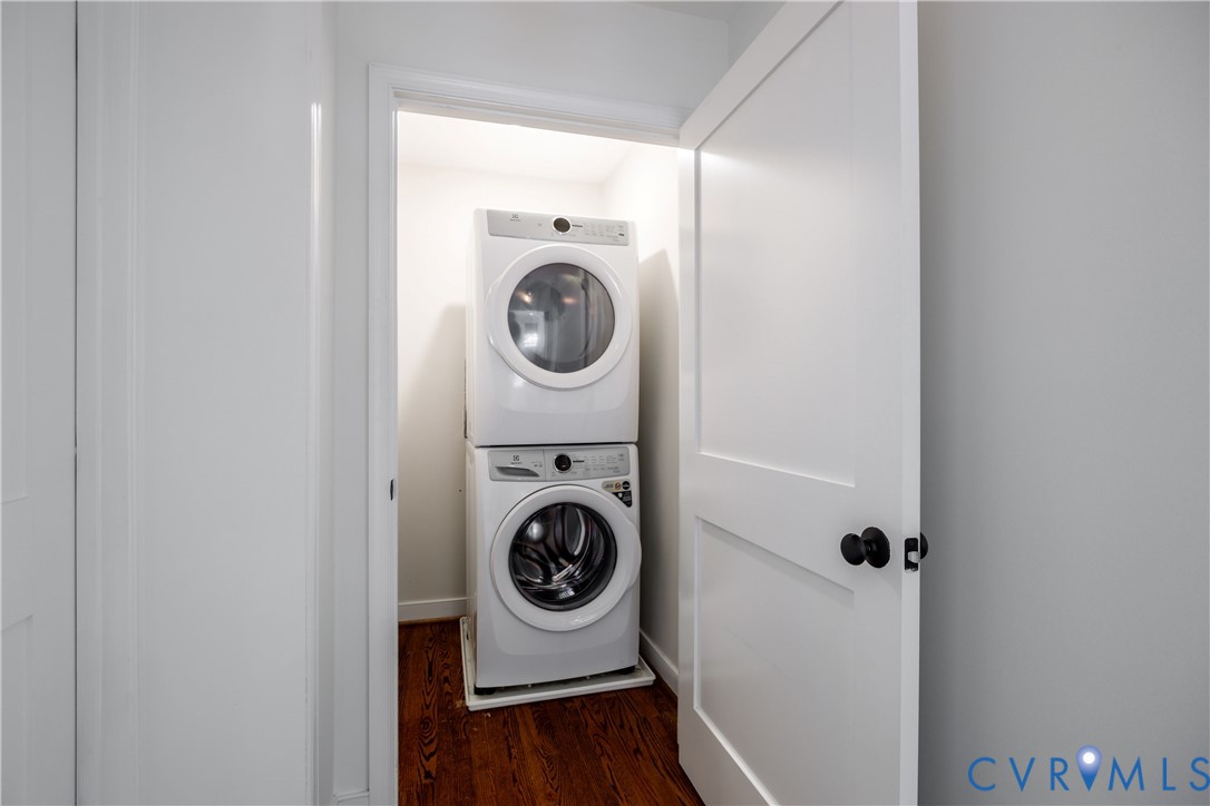 Stackable washer and dryer appliances within a dedicated closet, featuring a paneled door and dark wood-finish flooring