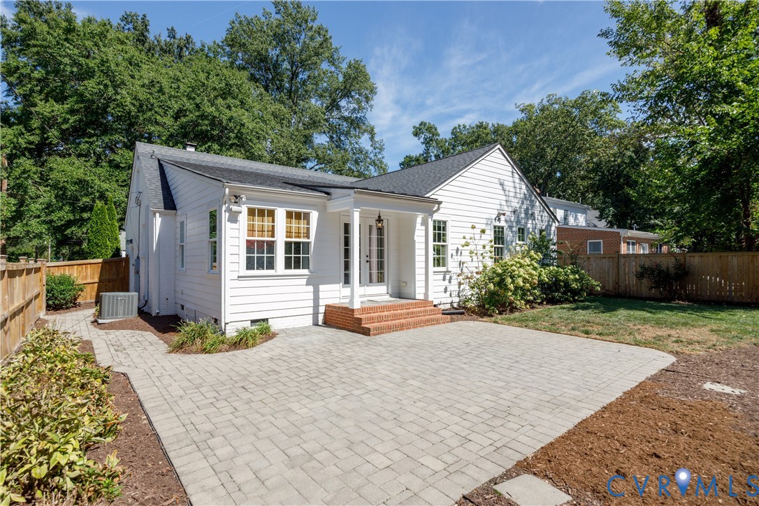White siding exterior with multiple windows, leading to a paver patio with a brick landing