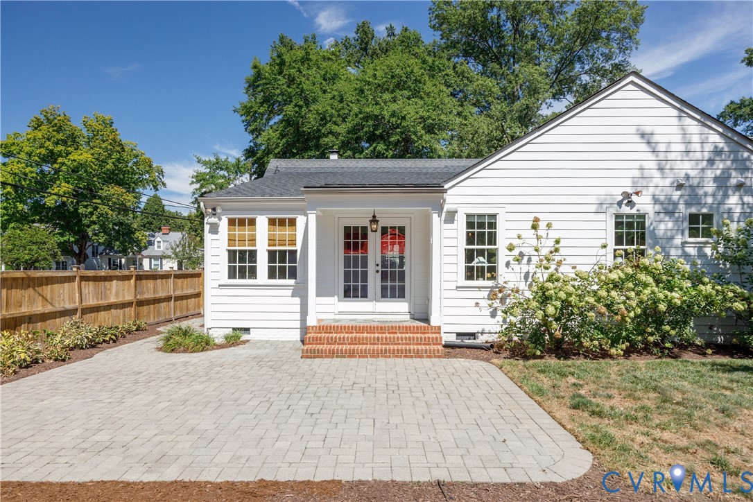 White siding exterior with multiple windows, a wood privacy fence, and a paver patio