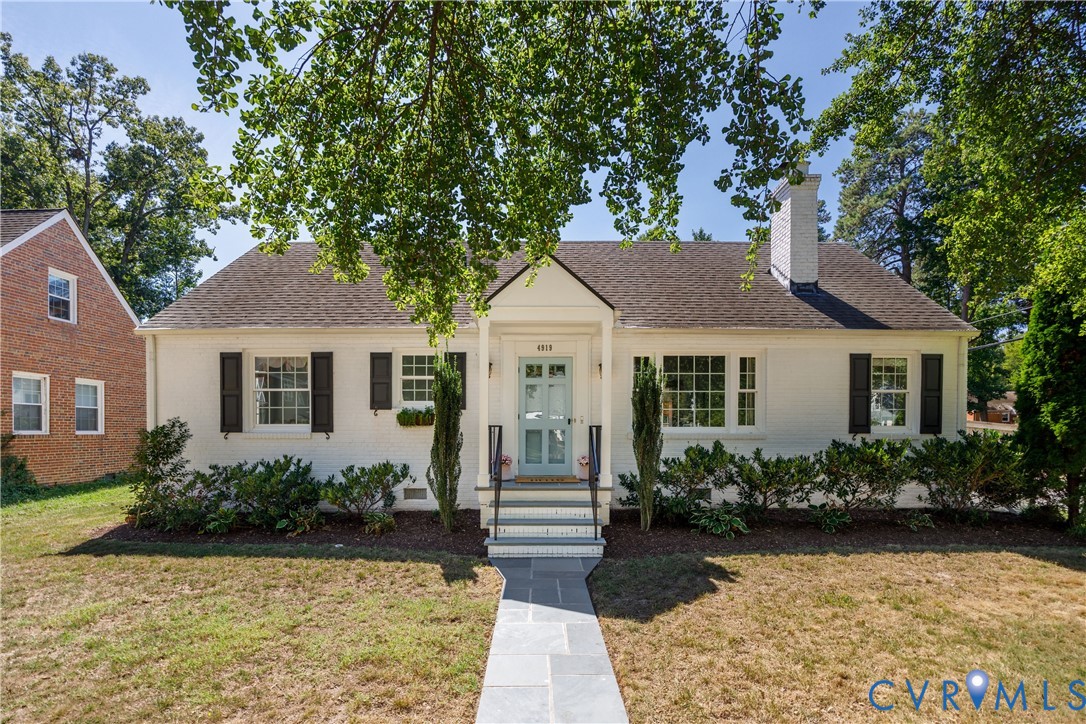 White painted brick exterior with black shutters, a light blue front door, a white chimney, and a stone walkway