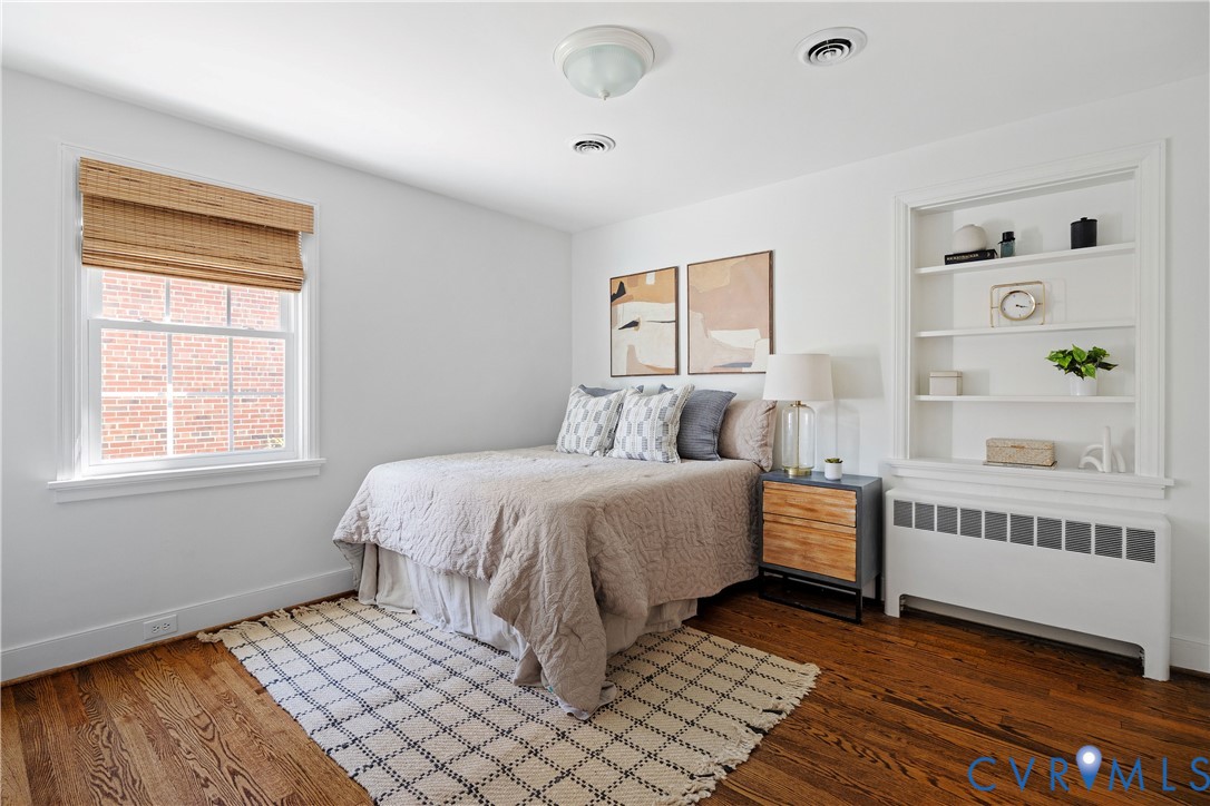 Hardwood flooring, built-in shelving, white walls, and a double-hung window