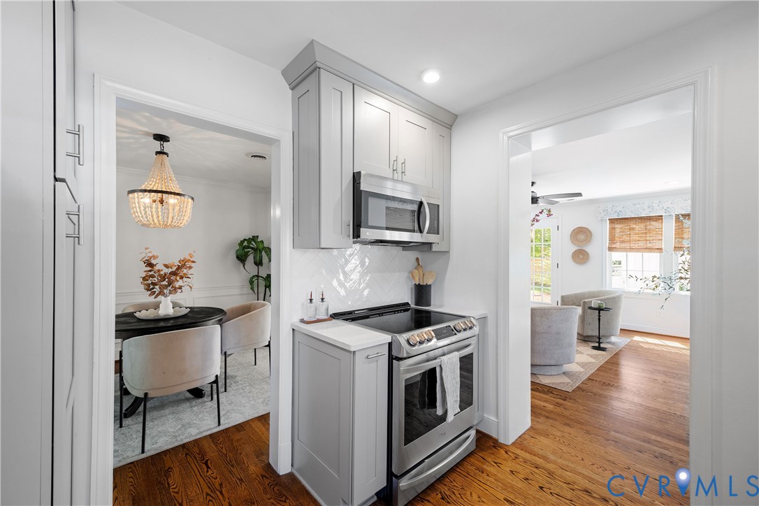 Stainless steel range with an overhead microwave, grey upper and lower cabinetry, and a white herringbone tile backsplash