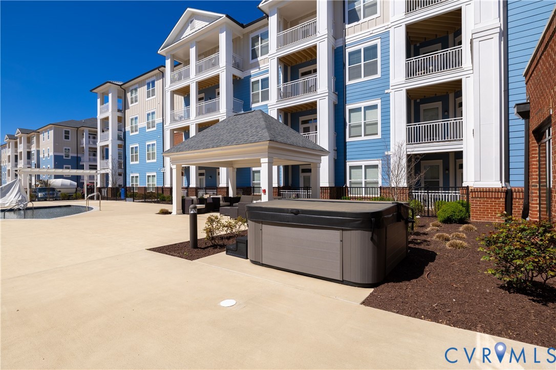 Outdoor hot tub, covered patio area, concrete hardscaping, landscaped planting beds, and multi-story residential buildings