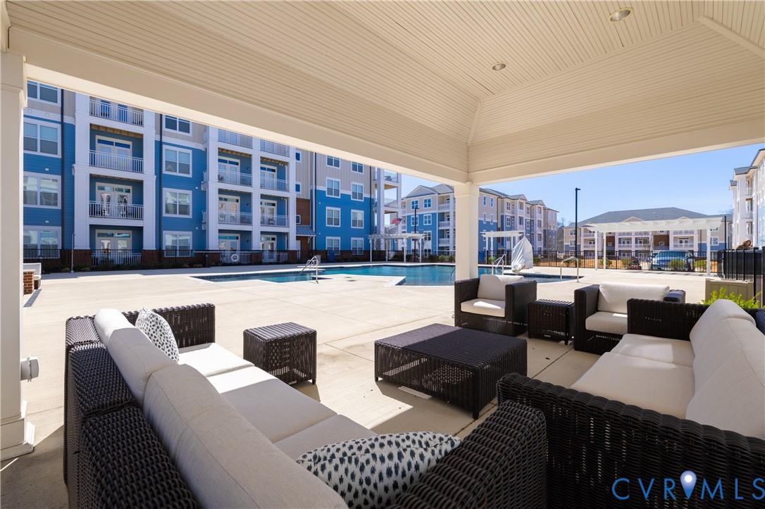 Covered outdoor patio with recessed lighting, an integrated swimming pool, and surrounding multi-story buildings