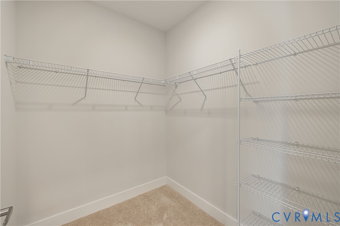 Walk-in closet with wire shelving system, wire hanging rods, and light-toned carpet flooring