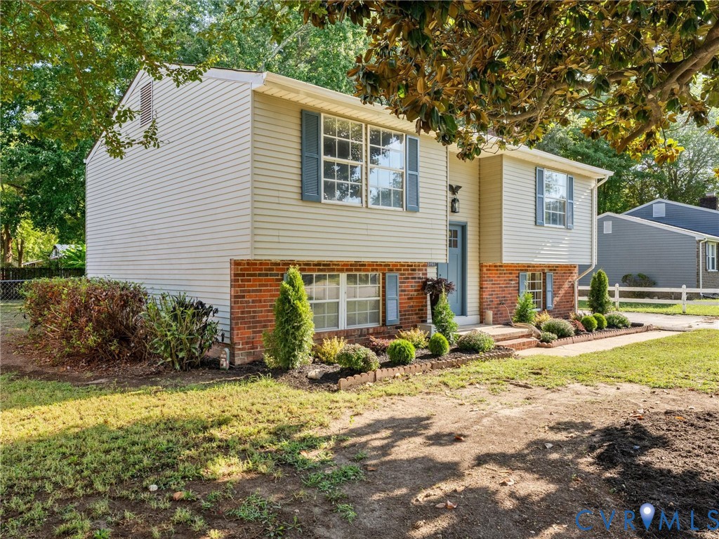 Split-level residence featuring brick and siding exterior, front door, multiple windows with shutters, and established landscaping