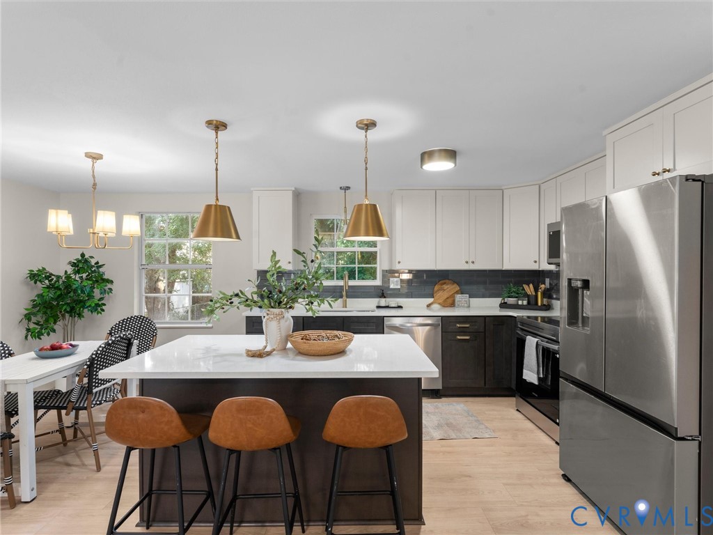 Kitchen featuring a center island with solid surface countertop, two-tone cabinetry, stainless steel appliances, and wood-finish flooring