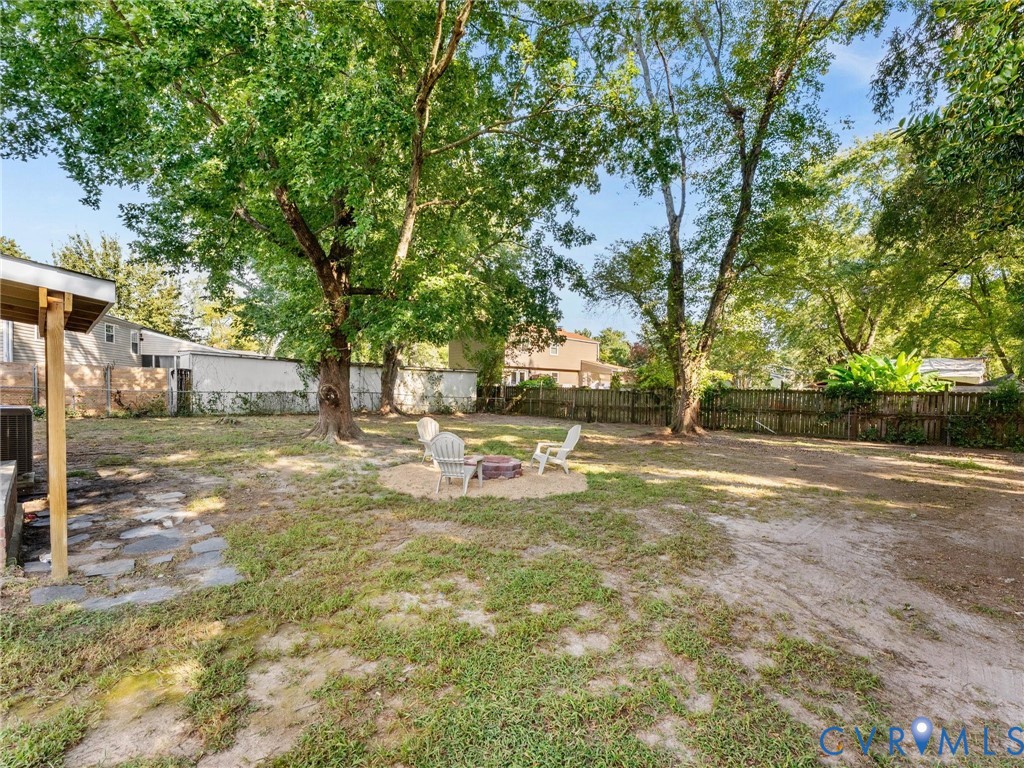 Expansive backyard featuring mature trees, a wood privacy fence, and a stone-paved patio area