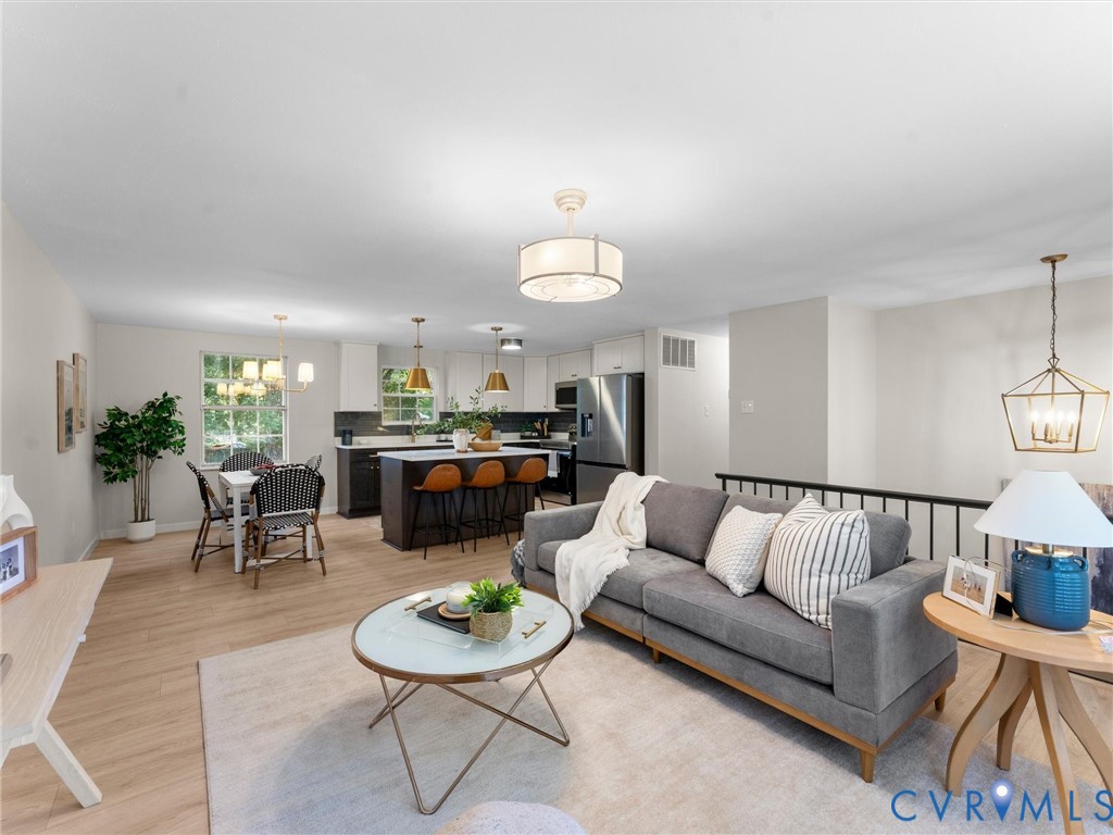 Open-concept living area with wood-finish flooring, a kitchen island with seating, pendant lighting, and a dining area with a window
