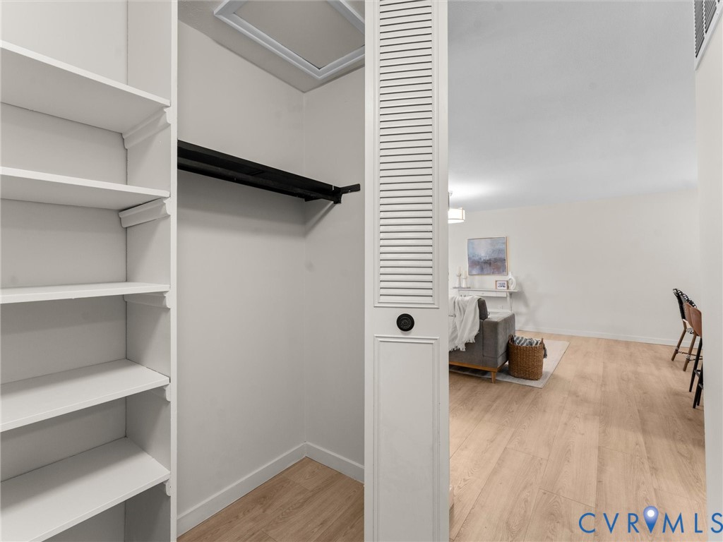 White shelving system, black closet rod, wood-finish flooring, white walls, louvered partition