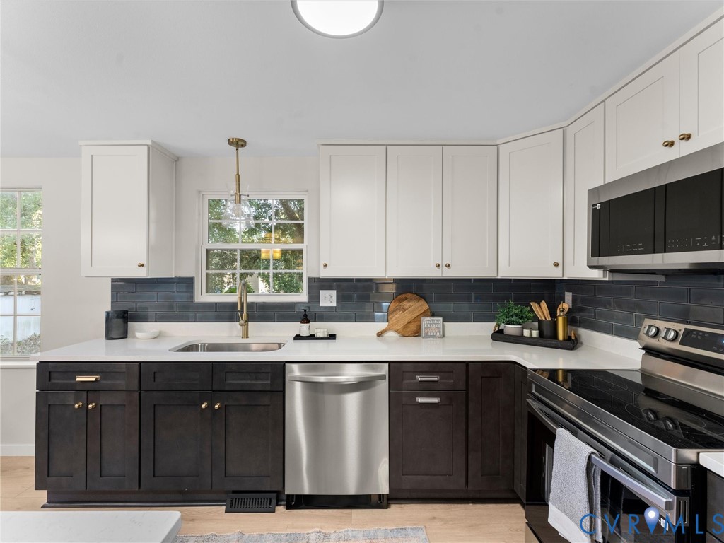Two-tone cabinetry with white upper and dark wood-finish lower cabinets, stainless steel appliances, white countertops, and a dark tile backsplash