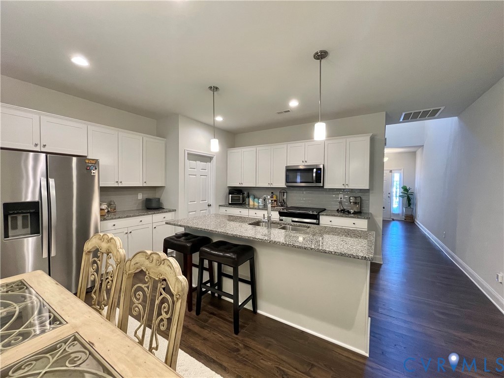 Kitchen featuring white cabinetry, stainless steel appliances, a center island with bar seating, and wood-finish flooring