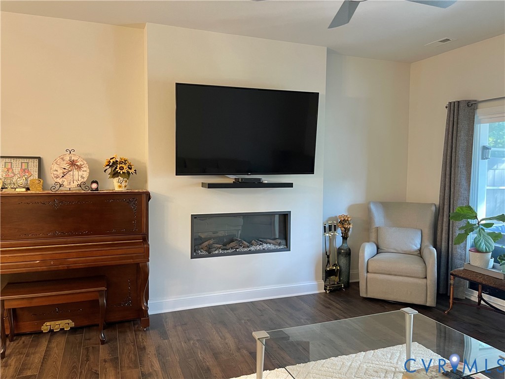 Wood-finish flooring, built-in electric fireplace, wall-mounted shelving, and ceiling fan