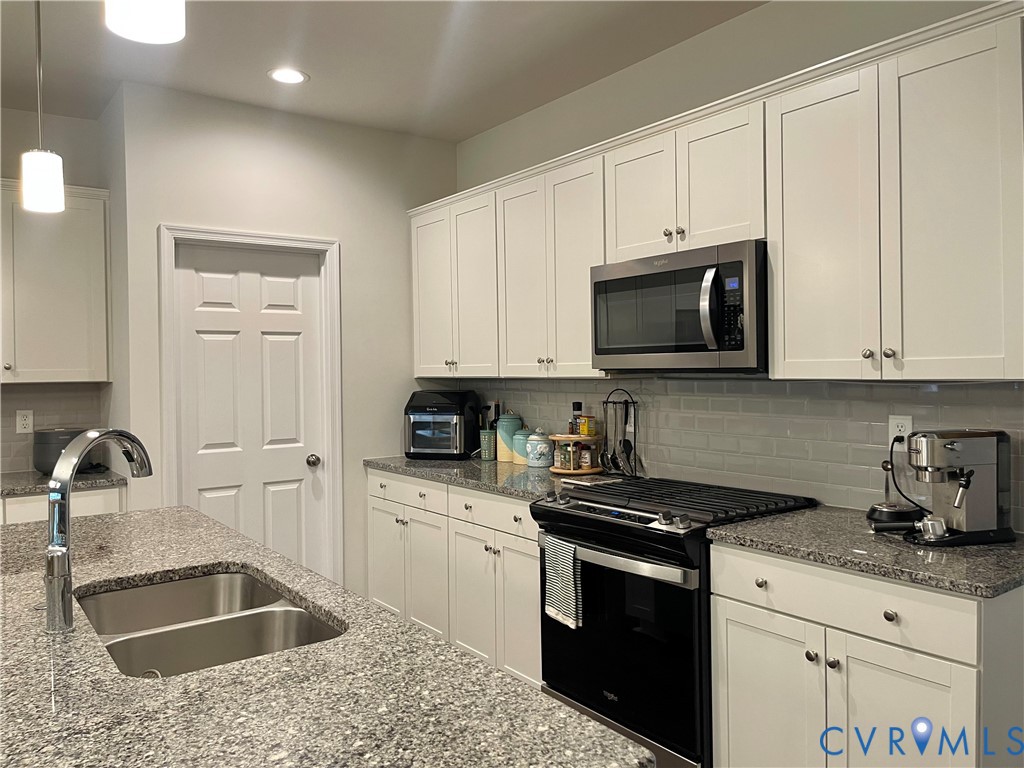Light-toned cabinetry, granite countertops, stainless steel appliances, a subway tile backsplash, and a double basin sink