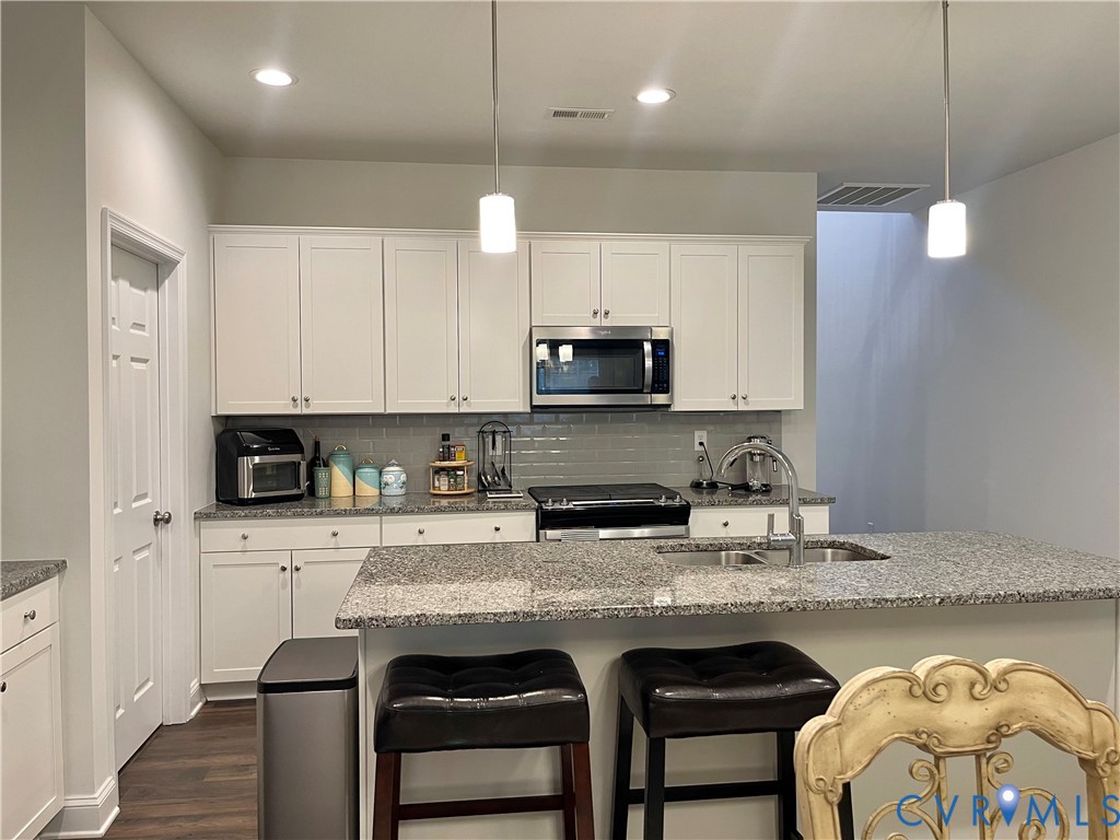 Spacious kitchen featuring white cabinetry, gray subway tile backsplash, stainless steel appliances, granite countertops, and an island with a stainless steel sink