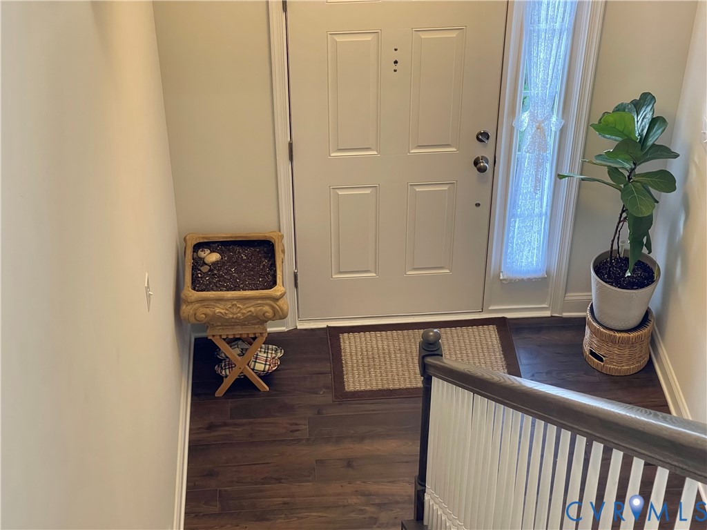 Entryway featuring a paneled door with sidelight, dark wood-finish flooring, and a staircase with white spindles and a wood handrail