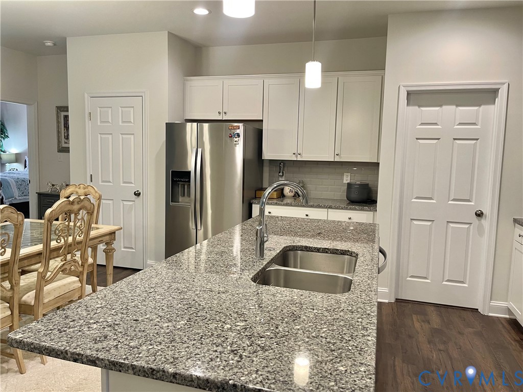 Kitchen featuring an island with a double basin stainless steel sink, light-toned countertop, white cabinetry, and stainless steel refrigerator